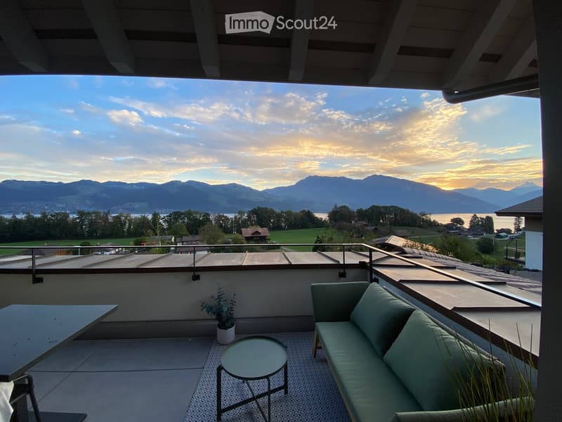 Roof terrace with a view of mountains and lake, featuring a green sofa, small round table, and potted plant.