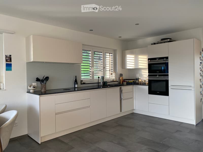 Modern kitchen with white cabinets, stainless steel appliances, and a black countertop. Features include an oven, sink, and various kitchen utensils.