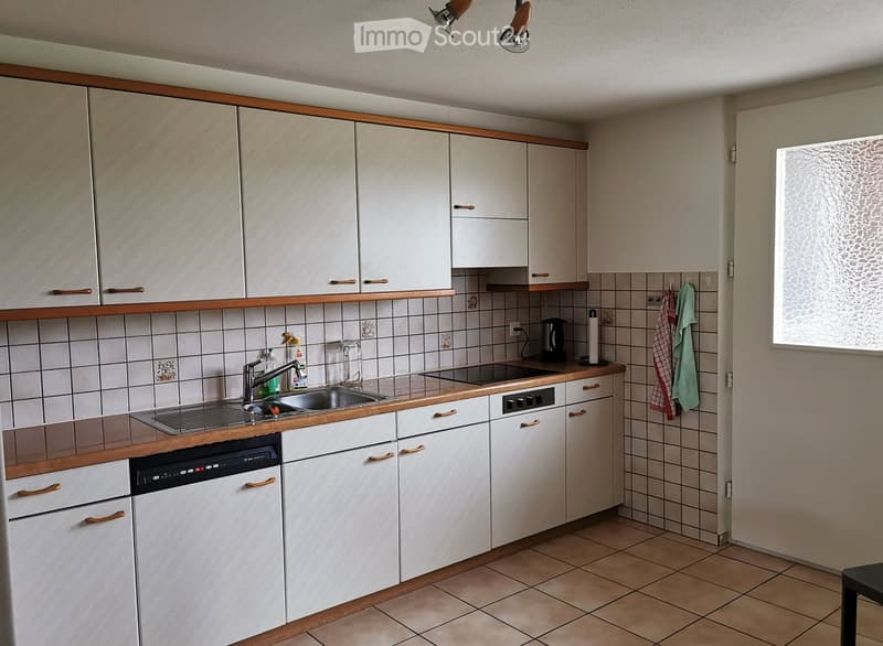 A modern kitchen with white cabinets, wooden countertops, a sink, a dishwasher, and various small appliances. The walls are tiled, and there is a window on the right side.