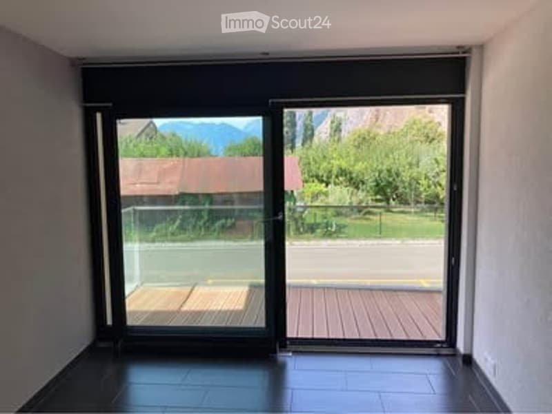 Empty room with large sliding glass doors leading to a balcony or terrace, offering a view of a house and greenery outside.