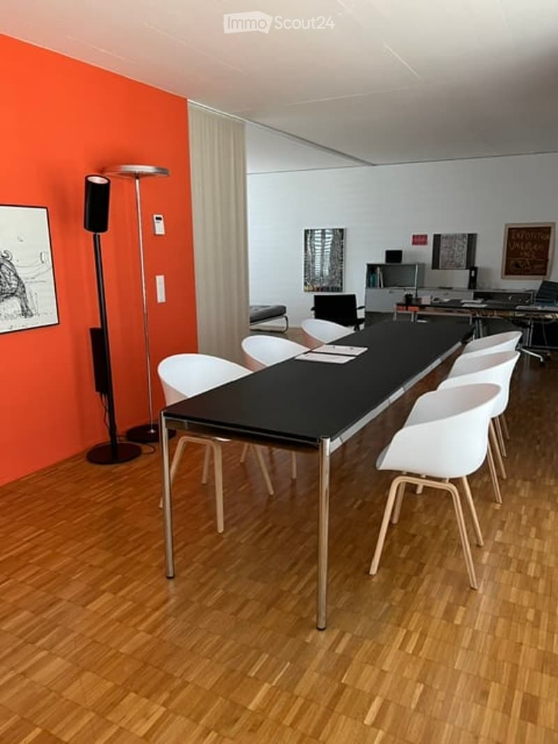 A modern conference room with a long black table, white chairs, a floor lamp, and multiple screens on the wall.