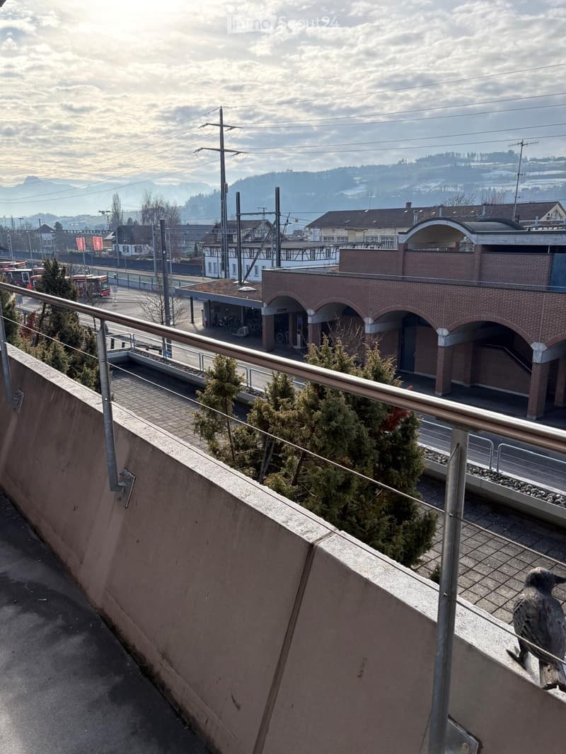 Balcony overlooking a cityscape with a brick building, metal railing, and a statue of a bird on the edge.