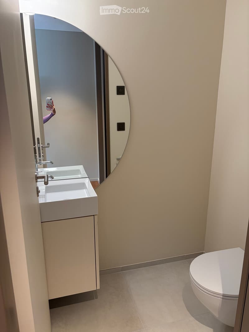 Modern bathroom with a white sink, toilet, and a round mirror on the wall.
