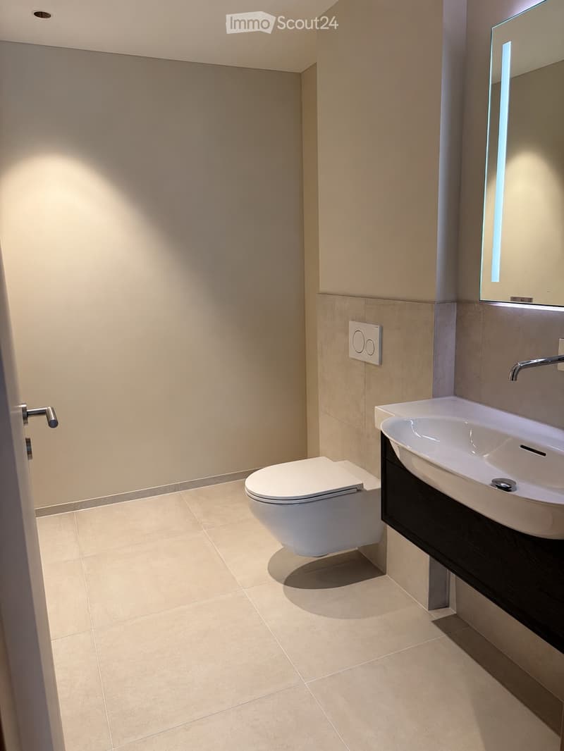 Modern bathroom with beige tiles, a white toilet, a sink with a modern faucet, and a large mirror above the sink.