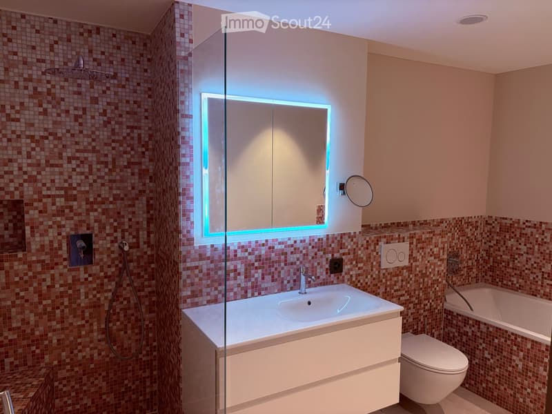 Modern bathroom with a white sink, mirror with LED lighting, toilet, bathtub, and a glass-enclosed shower area with a rainfall showerhead.