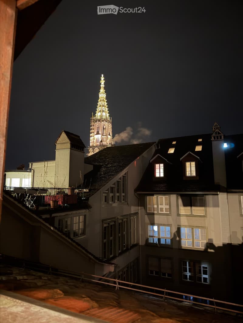 Nighttime view of a cityscape featuring a prominent illuminated tower with a spire and surrounding residential buildings with lit windows.
