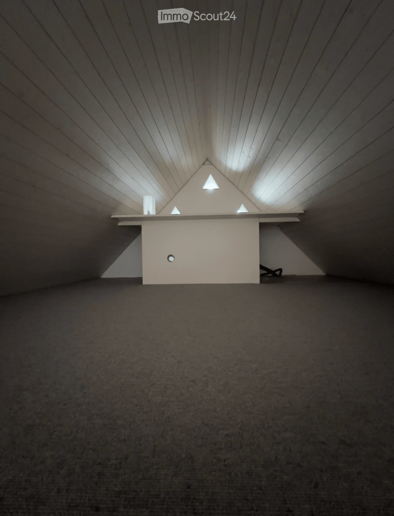 An empty room with a slanted wooden ceiling and a small white table with built-in lighting, featuring a dark carpeted floor.