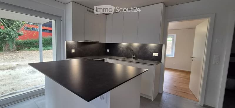 Modern kitchen with white cabinets, black countertop, and a kitchen island. The space features a sink with a faucet and an open doorway leading to another room.