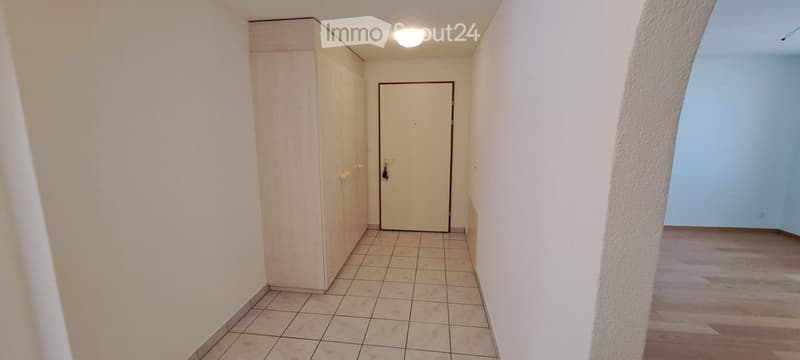 Empty hallway with tiled floor, white walls, a closed door, and a built-in closet on one side.