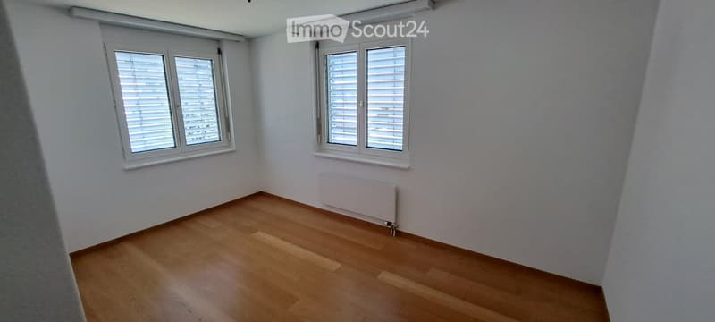 Empty room with wooden flooring, white walls, and two windows with blinds. No furniture or equipment present.