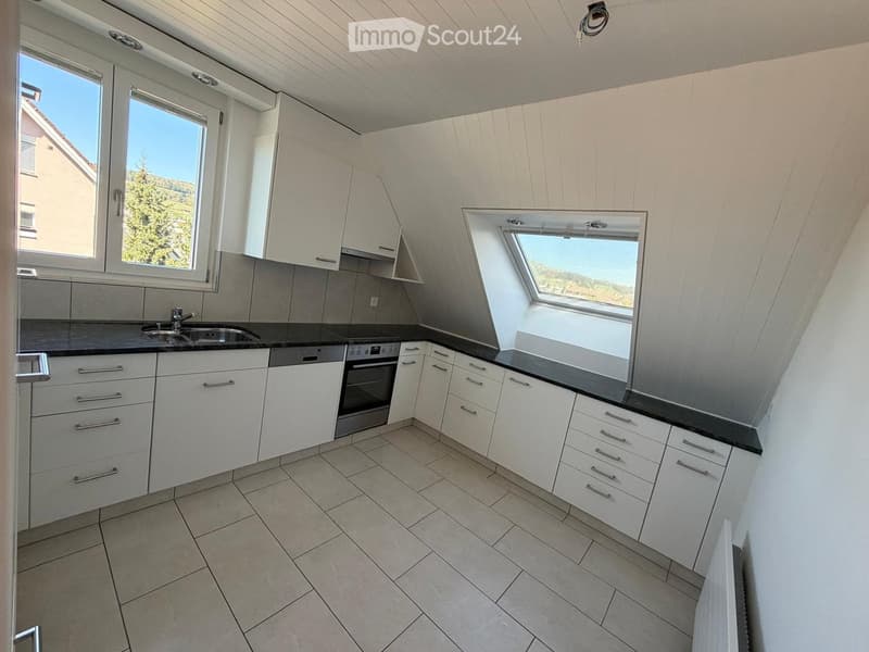 Modern kitchen with white cabinets, stainless steel sink, oven, and tiled floor. Features large windows and a skylight offering natural light.