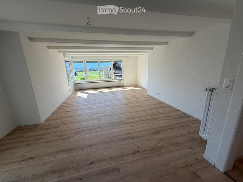 Empty room with wooden flooring, white walls, large windows offering a scenic view, and a radiator on one wall.