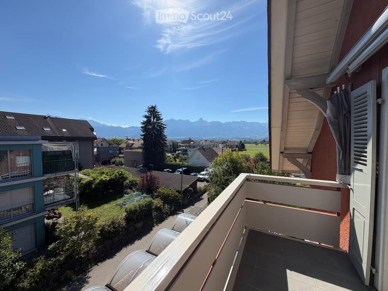 Balcony with a view of a suburban neighborhood, green spaces, and distant mountains under a clear blue sky.