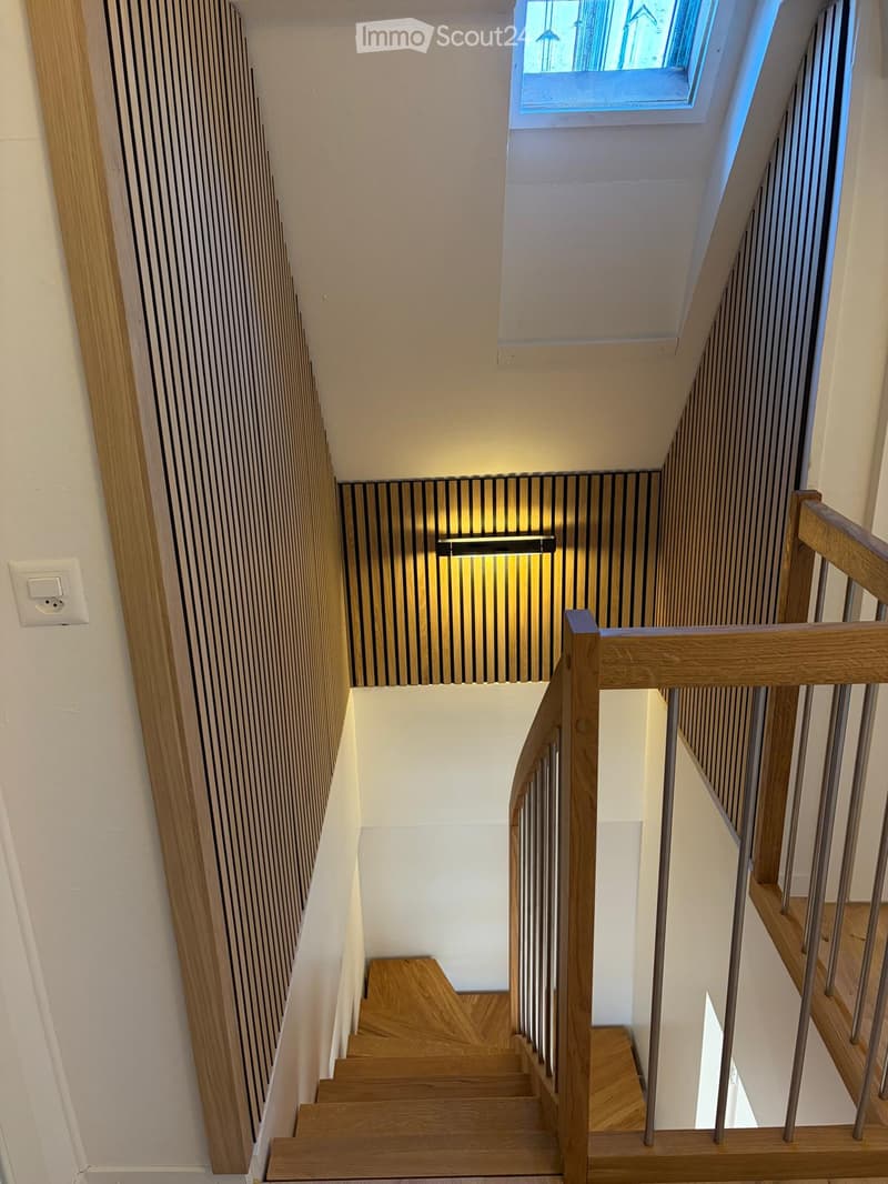 Wooden staircase with metal railing, modern lighting fixture, and a skylight at the top.