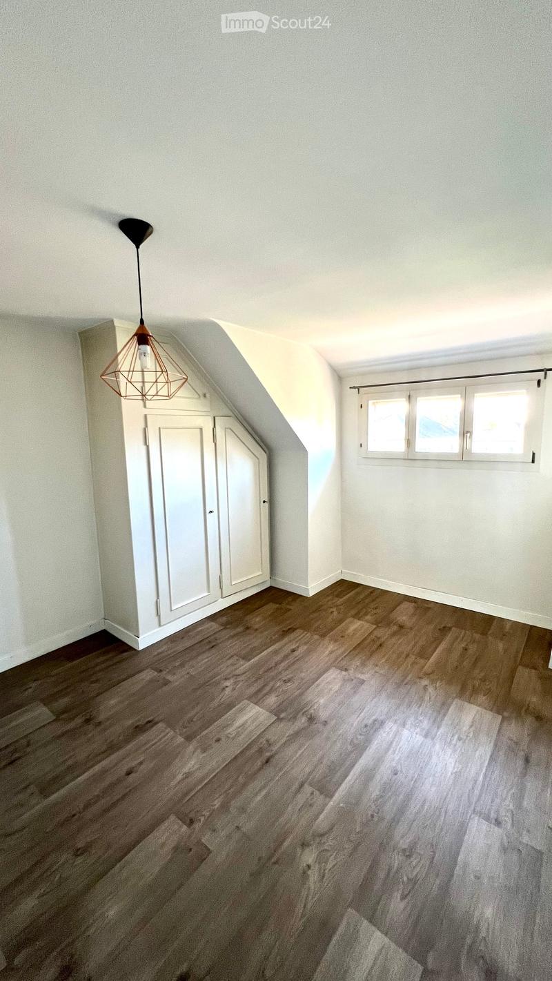 An empty attic room with wooden flooring, white walls, and a built-in closet. The room features a skylight window and a modern pendant light fixture.