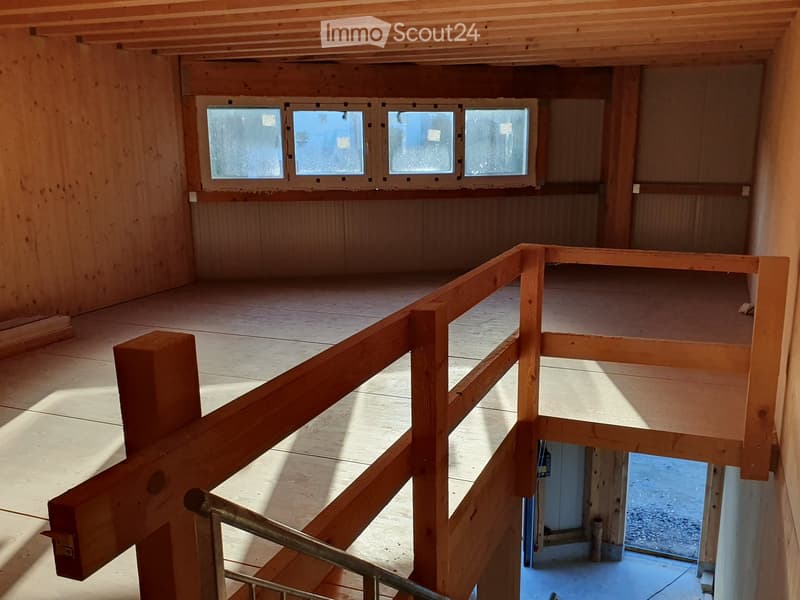 Empty wooden loft space with exposed beams, wooden floor, and large windows allowing natural light. No furniture or furnishings present.
