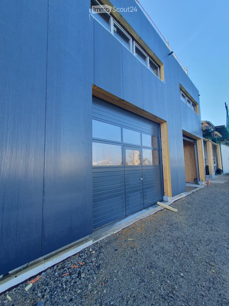 Modern two-story building with blue siding, large garage door, and visible construction materials on the right side.