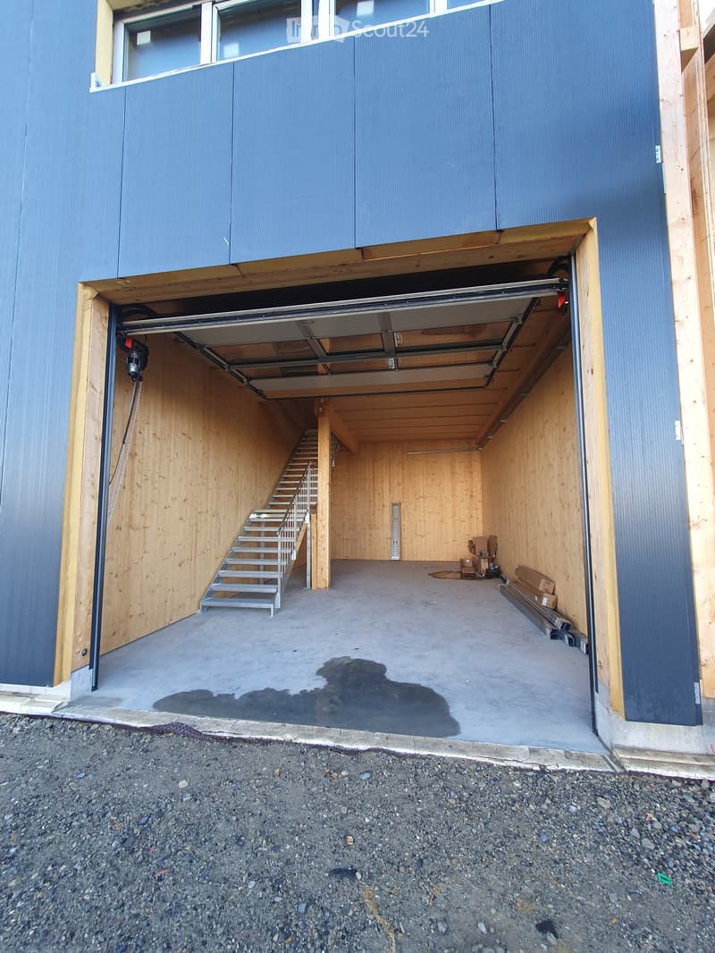 Open garage with wooden walls, metal staircase leading to an upper level, and some stored items inside.
