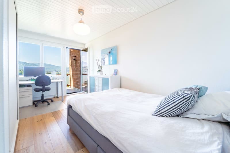 Bright bedroom with a large bed, desk with chair, and a view of the mountains through large windows and a sliding door.