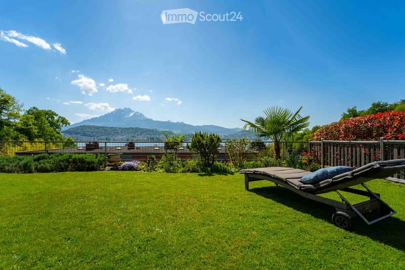 A well-maintained garden with a sun lounger, lush green grass, and a scenic mountain view in the background.