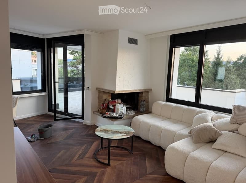 Modern living room with large windows offering a scenic view, a fireplace, a white sectional sofa, and a round coffee table.