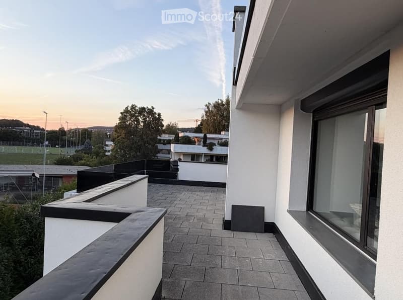 Modern balcony with tiled flooring, black railings, and expansive view of surrounding area and buildings.