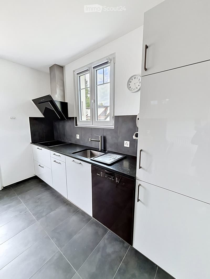 Modern kitchen with white cabinets, black countertops, stainless steel sink, dishwasher, and a window above the sink.