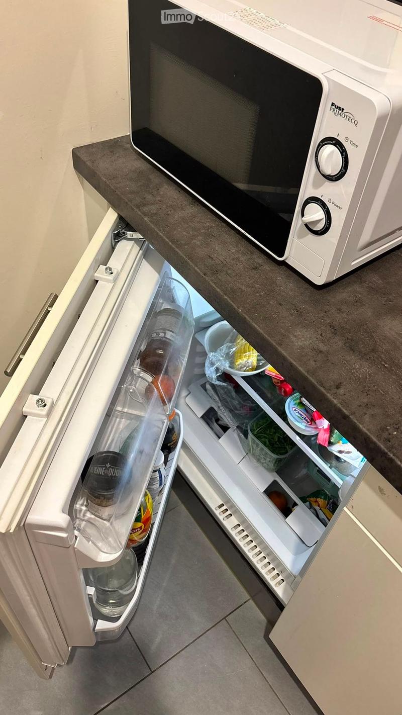 Open refrigerator with various items inside, including bottles, cups, and dishes, placed on a kitchen counter next to a microwave.
