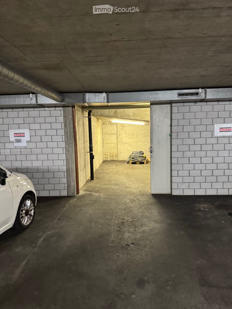 Underground parking area with concrete walls, tiled sections, and a parked car visible on the left side.