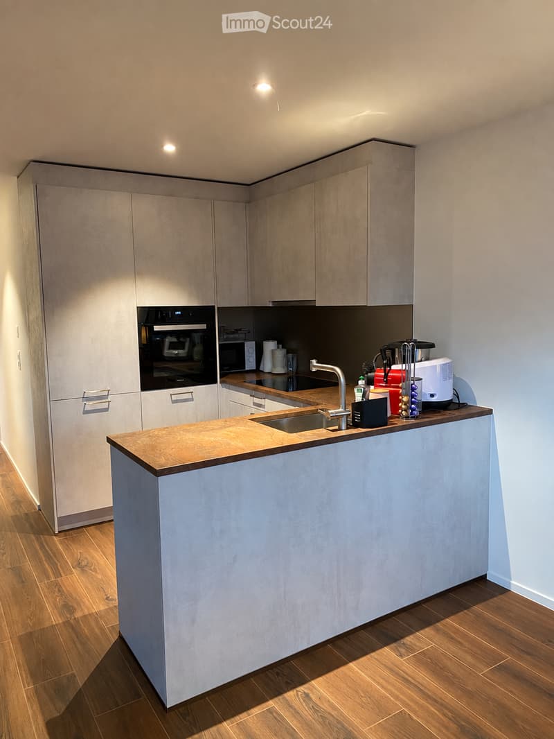 Modern kitchen with light wood cabinets, a central island, and various appliances including a sink, oven, and microwave.