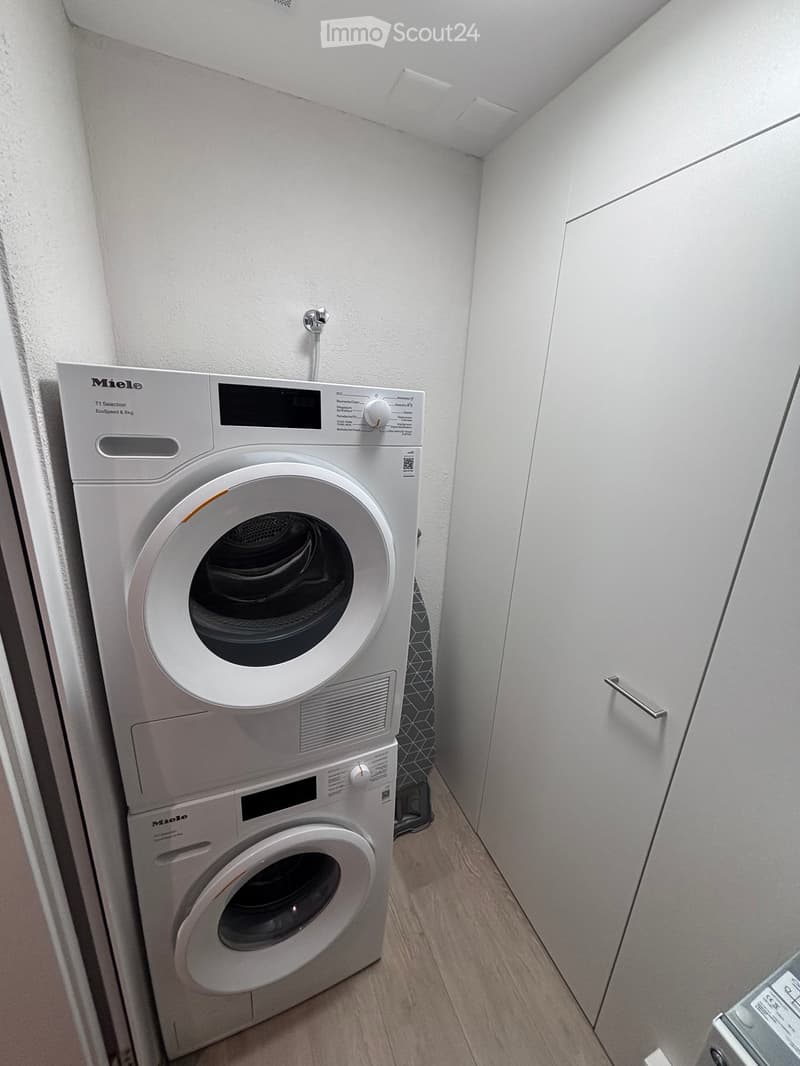 Compact bathroom with a stacked washing machine and dryer unit, white walls, and light wooden flooring.
