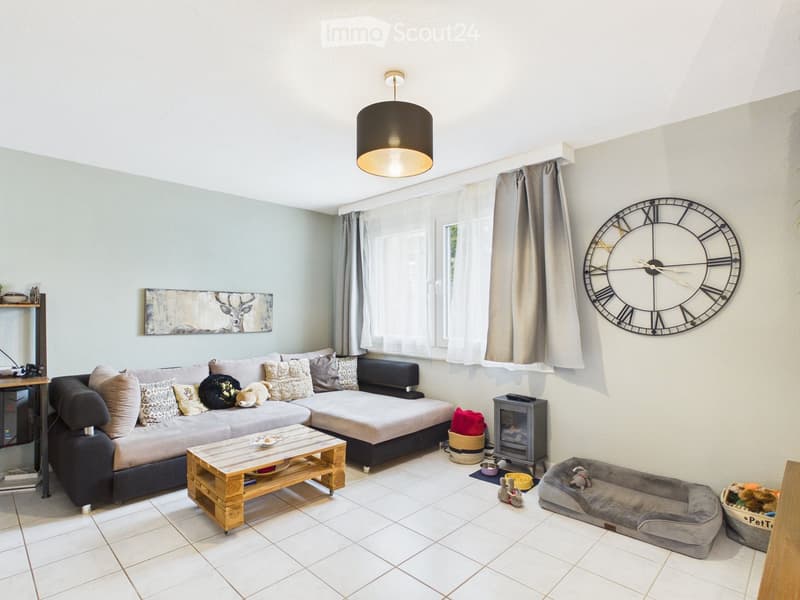 Living room with a grey sectional sofa, wooden coffee table, fireplace, dog bed, large wall clock, and artwork on the wall.