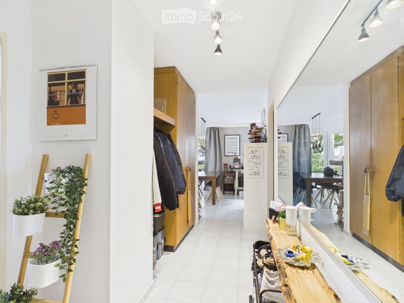 Bright hallway with white tiled flooring, wooden coat rack, small potted plants, and a wooden bench with shoes and cups.