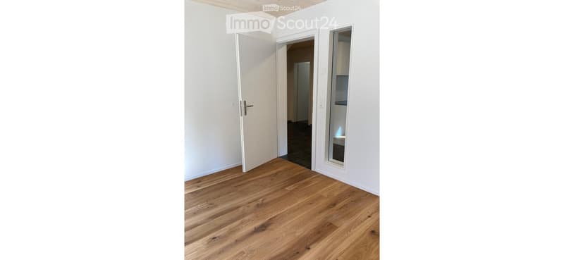 Empty room with wooden flooring, white walls, and two open doors leading to adjacent spaces.