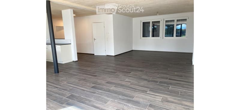 Empty room with dark wooden flooring, white walls, and large windows. No furniture or equipment present.