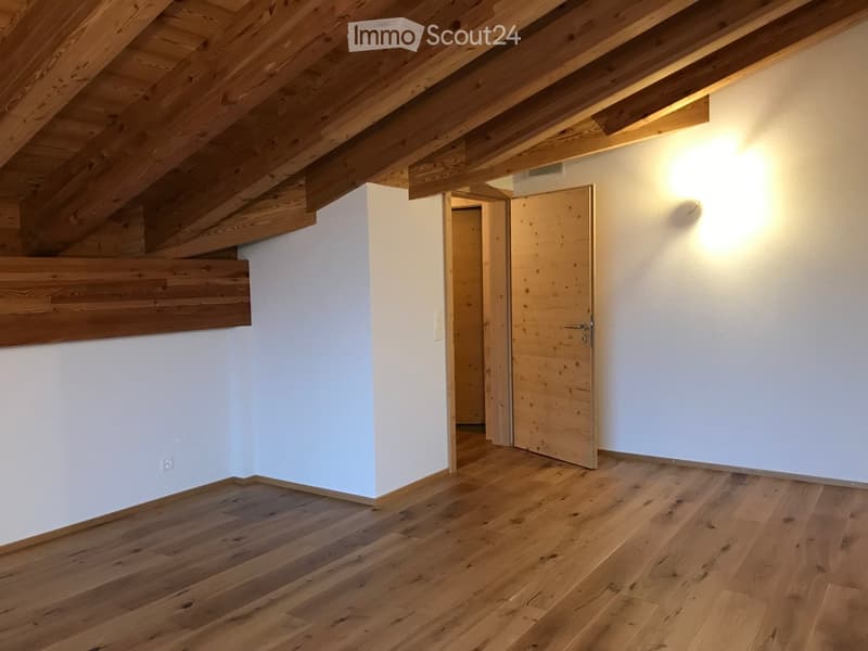 Empty room with wooden floors, white walls, and exposed wooden beams on the ceiling. A wooden door is open, leading to another space.