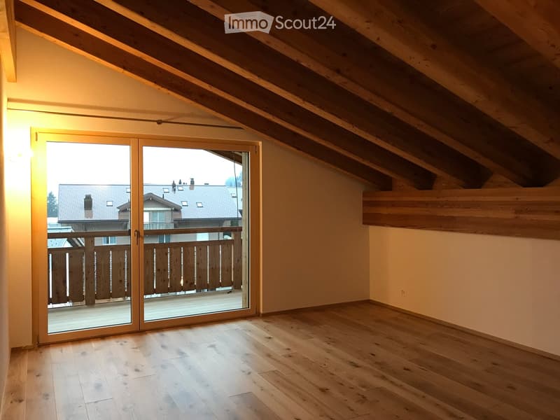 Bright, empty attic room with wooden floors, exposed wooden beams, and large sliding glass doors leading to a balcony.