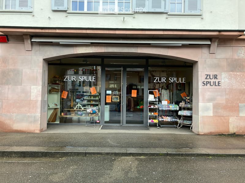 Storefront of a shop with glass doors and windows, name board 'ZUR SPULE', displayed products and banners