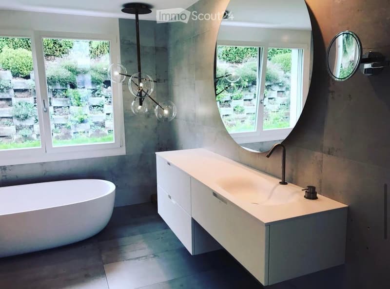 Modern bathroom with a freestanding bathtub, a floating sink vanity, a large round mirror, and a stylish chandelier with glass globes.