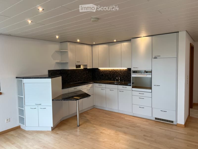 Modern kitchen with white cabinets, granite countertops, and stainless steel appliances including a sink, oven, and refrigerator. The space features wooden flooring and recessed lighting.