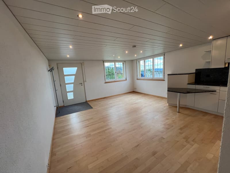 Empty room with light wooden flooring, white walls, and large windows. Features a door with glass panels and a small rug near the entrance.