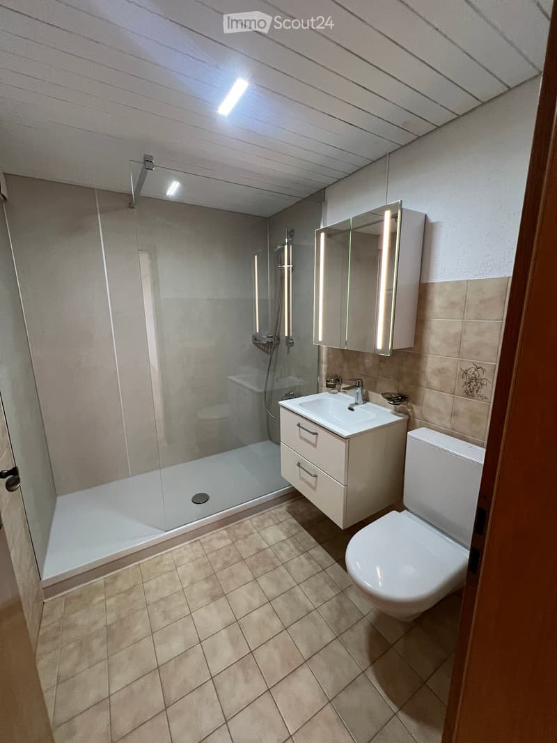 Modern bathroom with tiled floor, white toilet, sink with cabinet, and glass-enclosed shower area.