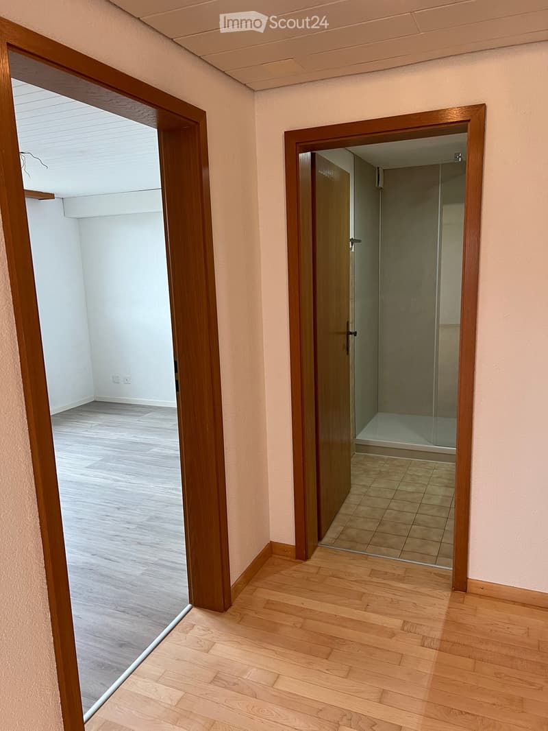 Empty hallway with wooden flooring and light-colored walls, featuring two open doors leading to other rooms.