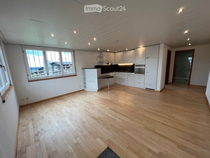 Empty room with light wooden flooring, white walls, and white cabinetry. Large windows provide natural light, and the space is unfurnished.