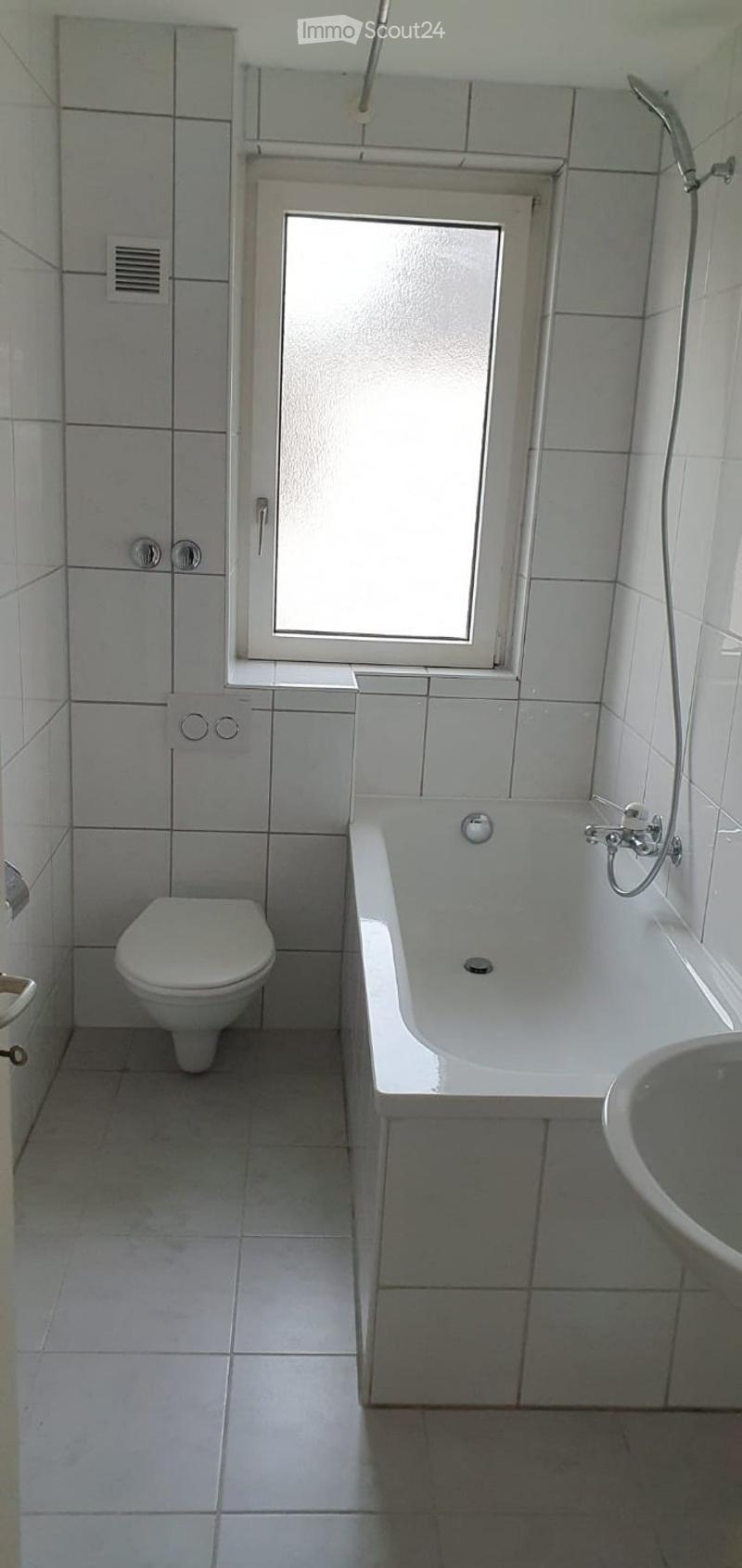Clean, modern bathroom with white tiles, a toilet, a bathtub, and a sink. Features a frosted window and a showerhead.