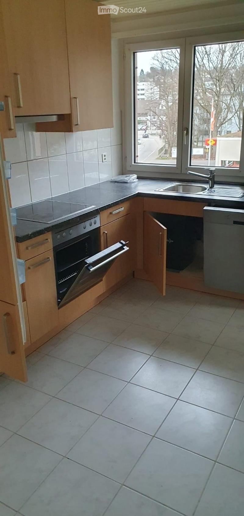 Modern kitchen with light wooden cabinets, tiled floor, stainless steel oven, and sink.