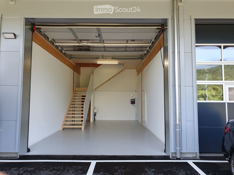 Modern garage with a wooden staircase leading to an upper level, white walls, and a large open space.