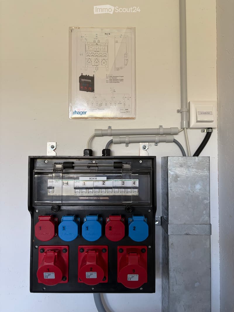 Electrical panel with multiple circuit breakers and labeled plugs, mounted on a wall with visible wiring and a schematic diagram above.
