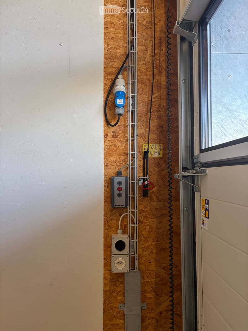 A narrow hallway with a wooden panel wall, electrical outlets, and a window on the right side.