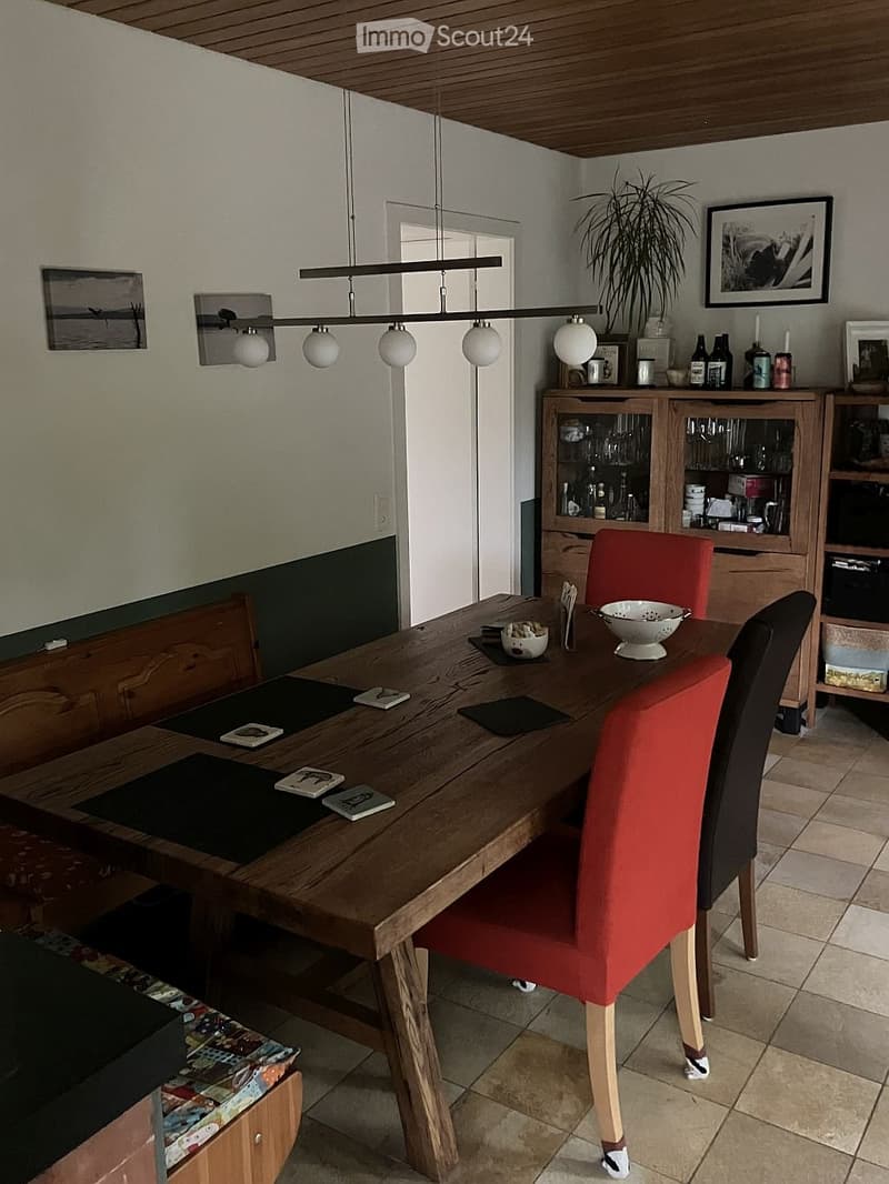 Dining room with a wooden dining table, red chairs, pendant light, and wooden cupboards with glass doors.